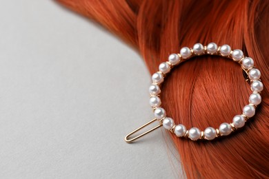 Elegant pearl clip and red hair strand on white background, closeup. Space for text