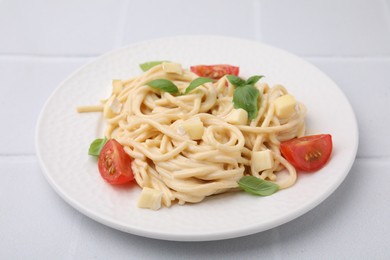 Delicious pasta with brie cheese, tomatoes and basil leaves on white tiled table, closeup