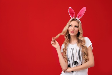 Photo of Portrait of beautiful young woman in Easter bunny ears headband on color background, space for text