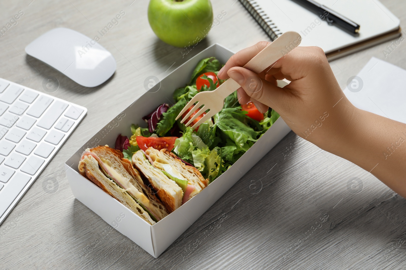 Photo of Office employee eating fresh salad with meat at white wooden table, closeup. Business lunch at workplace