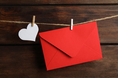 Red envelope and paper heart hanging on twine against wooden background. Love letter