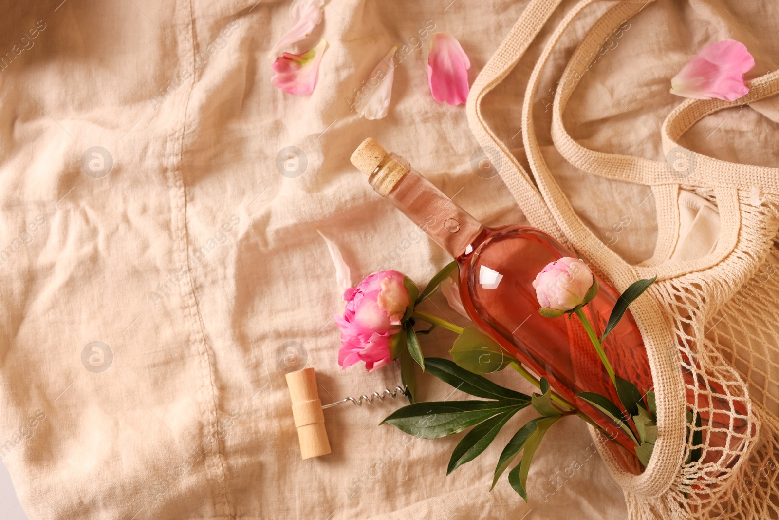 Photo of Flat lay composition with rose wine and beautiful peonies on beige fabric. Space for text