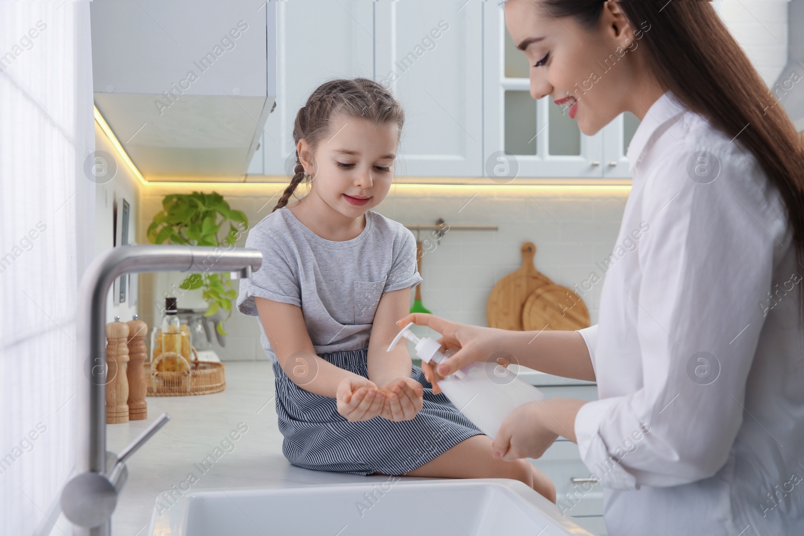 Photo of Mother and daughter washing hands with liquid soap together in kitchen