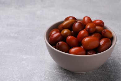 Photo of Fresh Ziziphus jujuba fruits in bowl on light table. Space for text