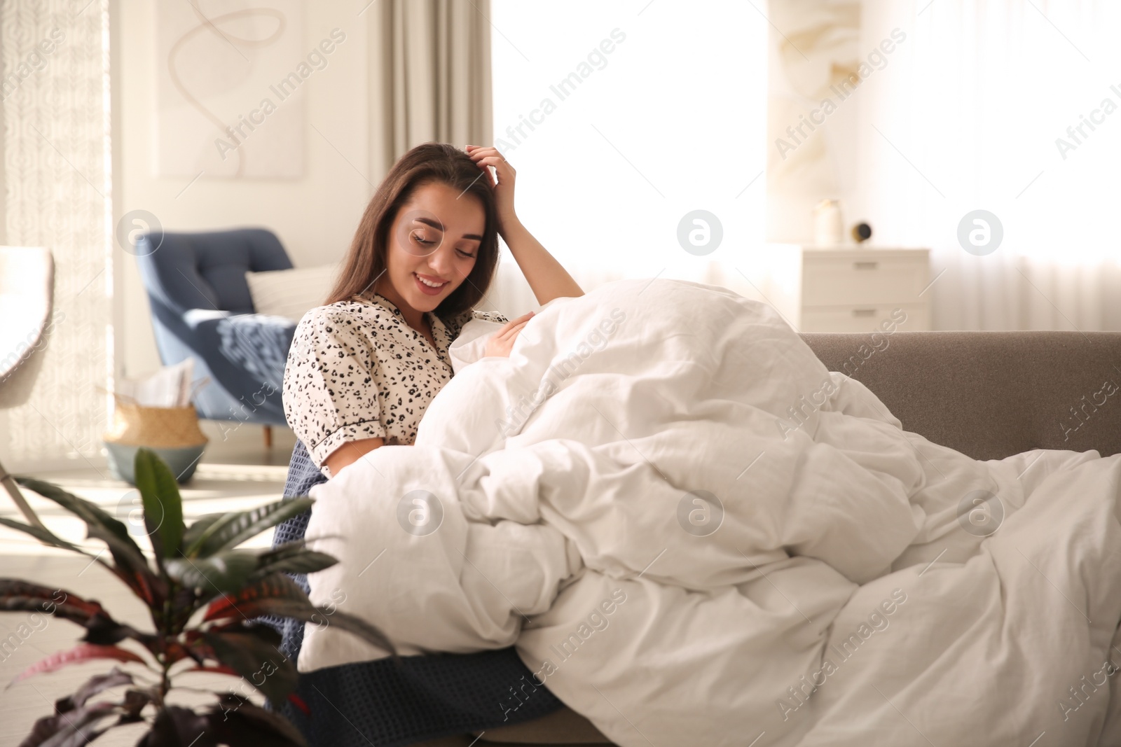 Photo of Beautiful young woman wrapped with soft blanket relaxing on sofa at home