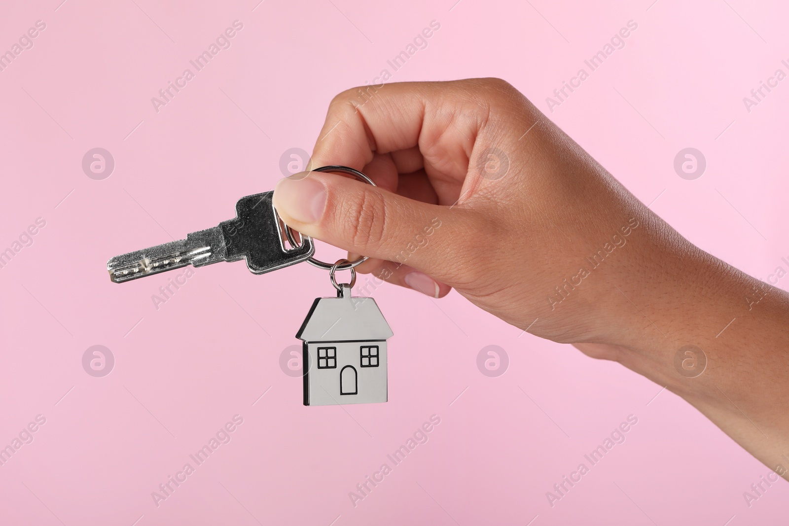 Photo of Woman holding key with metallic keychain in shape of house on pink background, closeup