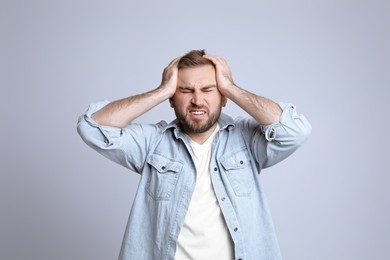 Young man suffering from headache on light background