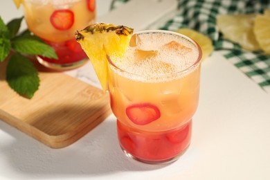 Photo of Spicy pineapple cocktail with chili pepper and ice cubes on white table, closeup
