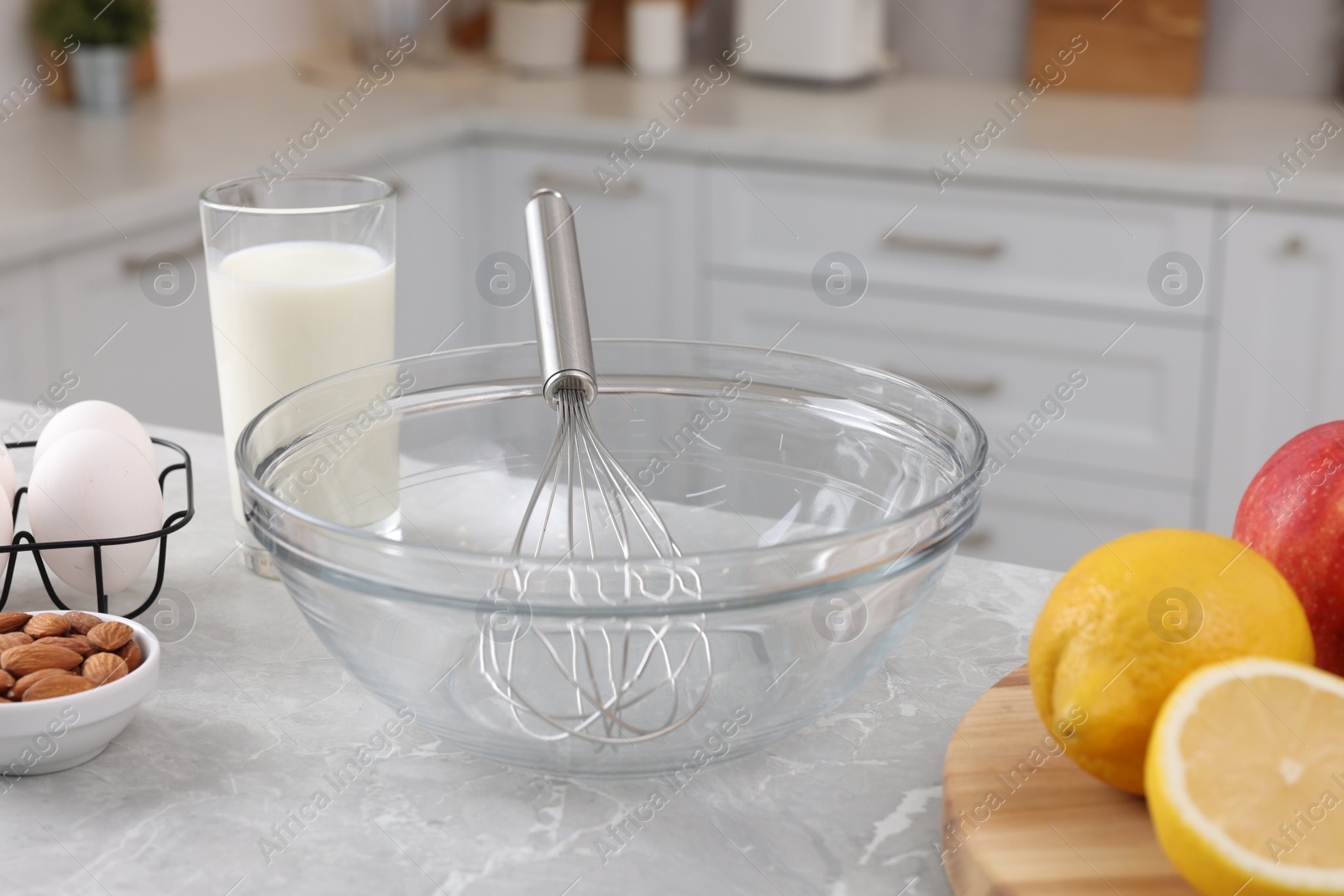 Photo of Metal whisk, bowl and different products on gray marble table in kitchen