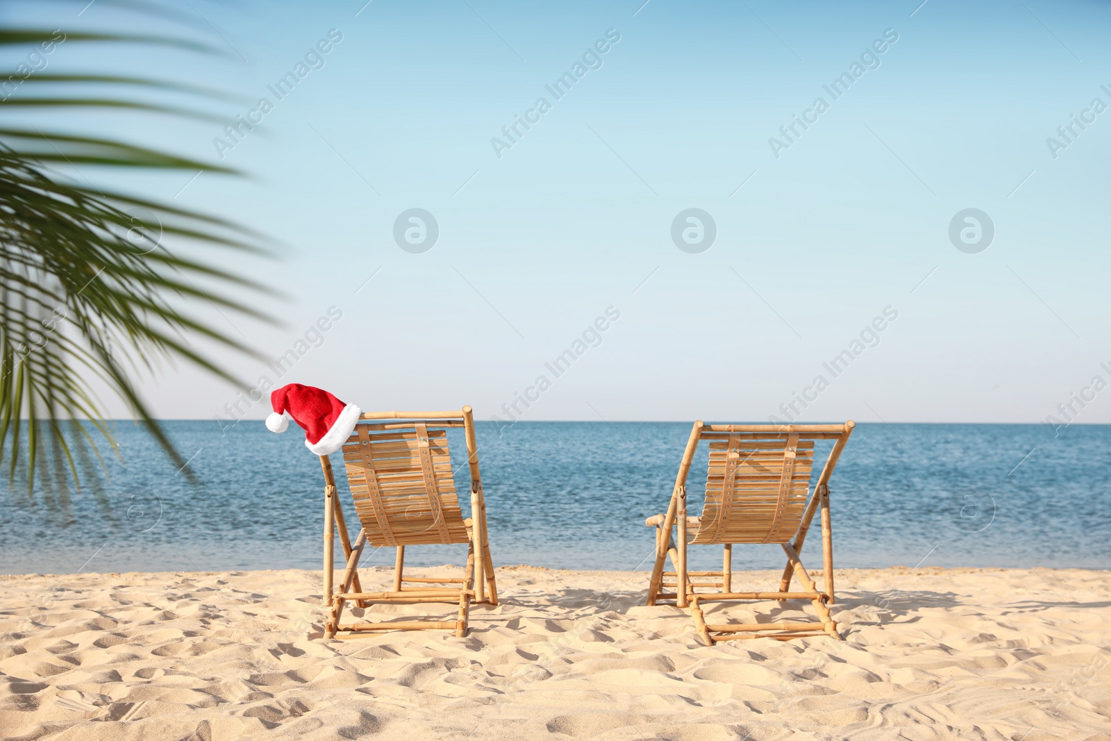 Photo of Sun loungers and Santa's hat on beach, space for text. Christmas vacation