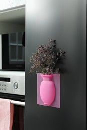 Silicone vase with beautiful violet flowers on fridge in kitchen