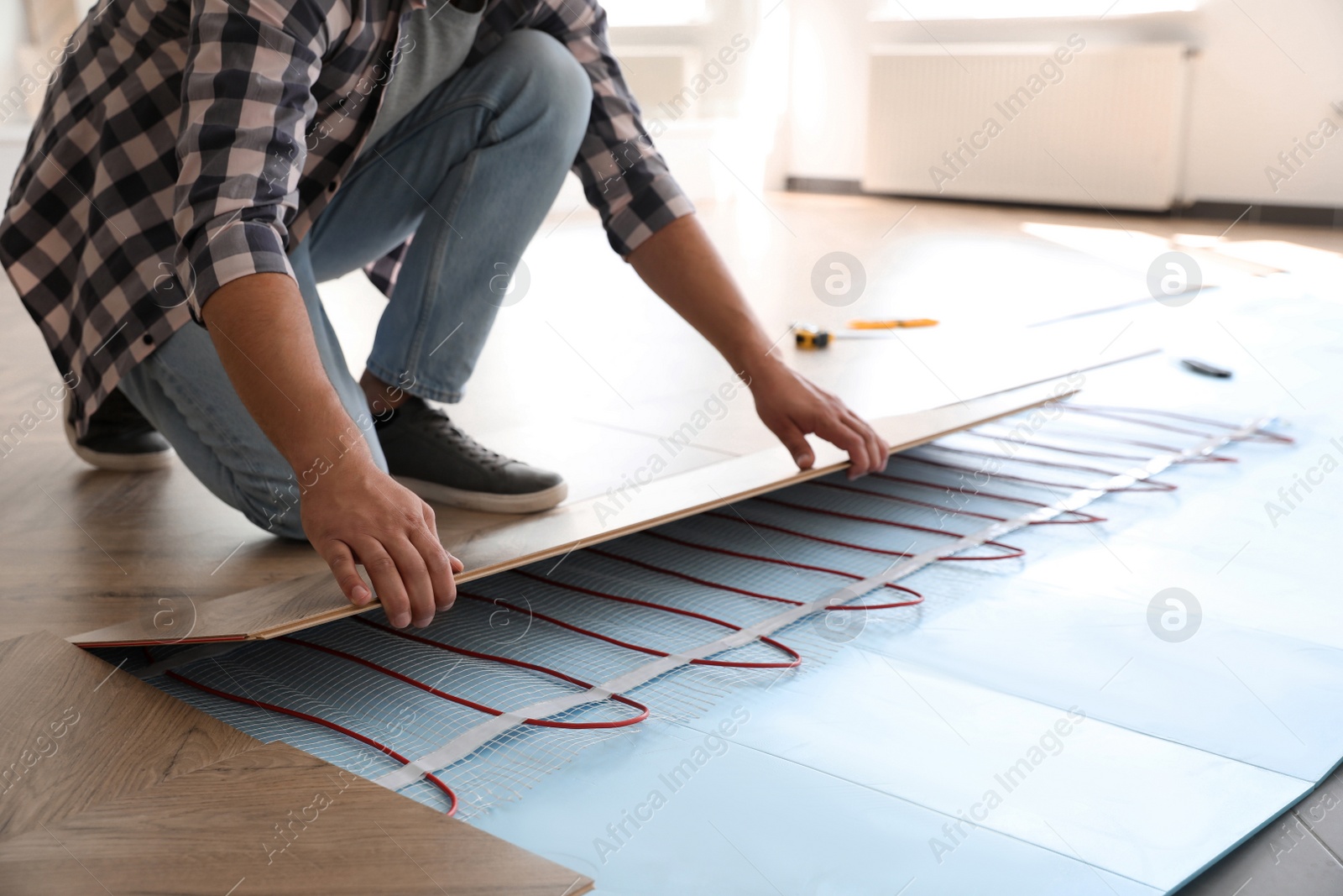 Photo of Professional contractor installing underfloor trace heating system indoors, closeup