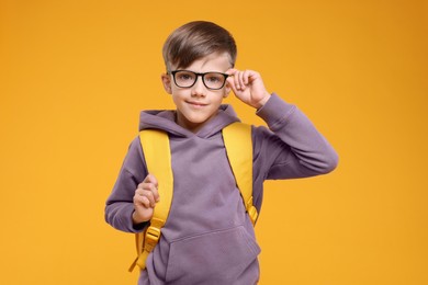 Photo of Cute schoolboy in glasses on orange background