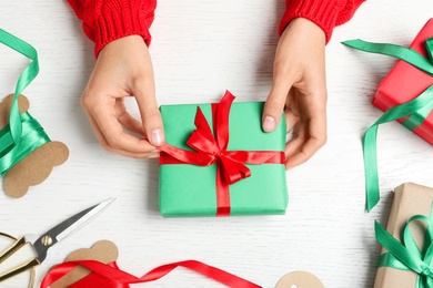 Photo of Woman wrapping Christmas gift at white wooden table, top view