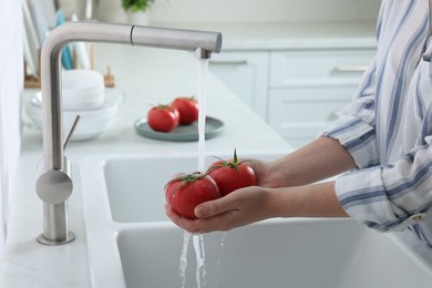 Photo of Woman washing fresh ripe tomatoes under tap water in kitchen, closeup