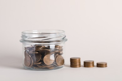 Glass jar with money and stack of coins on white background, closeup