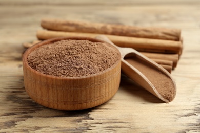 Photo of Aromatic cinnamon powder and sticks on wooden table, closeup