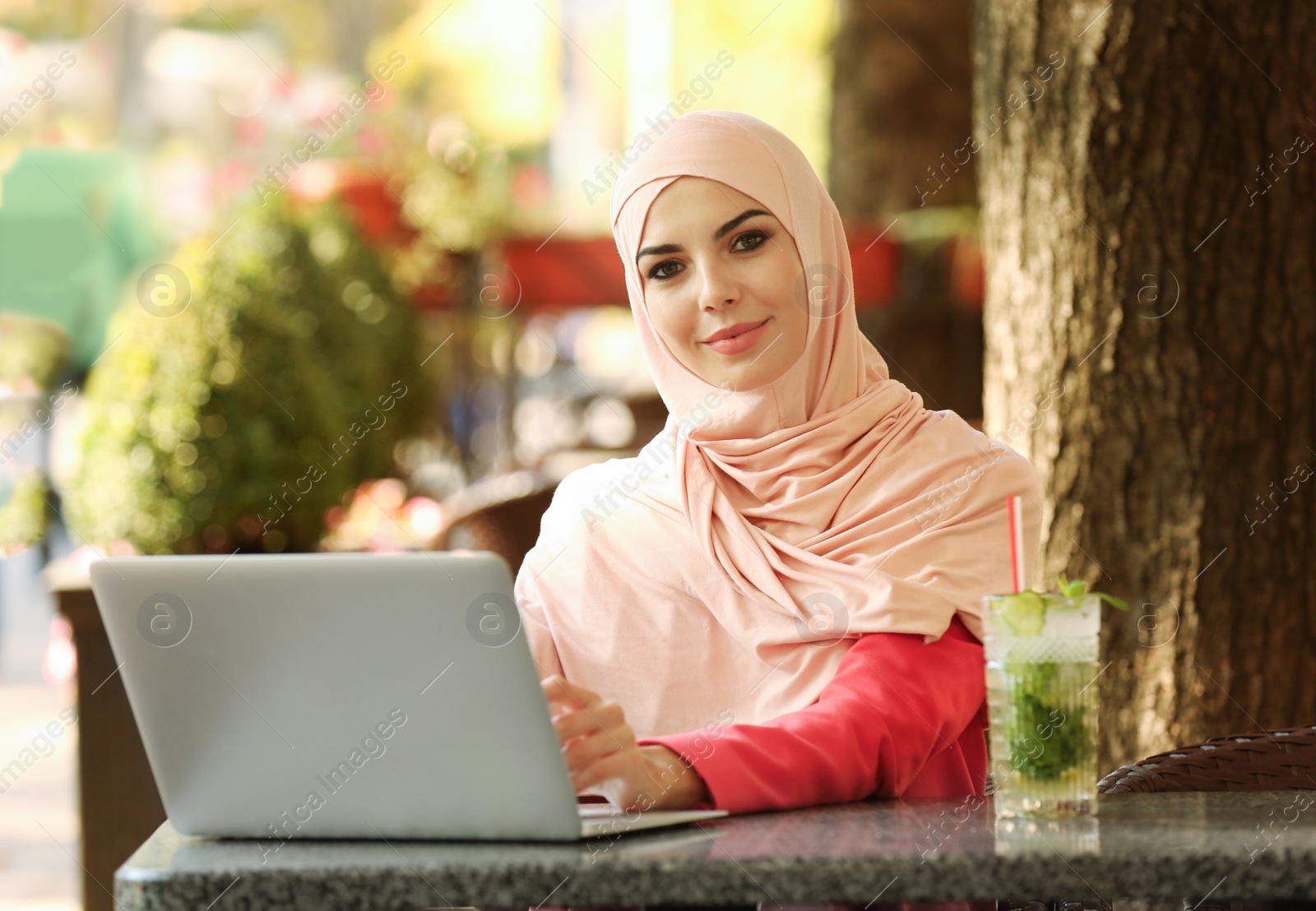 Photo of Muslim woman using laptop in outdoor cafe