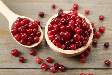 Photo of Fresh ripe cranberries in bowl and spoon on wooden table