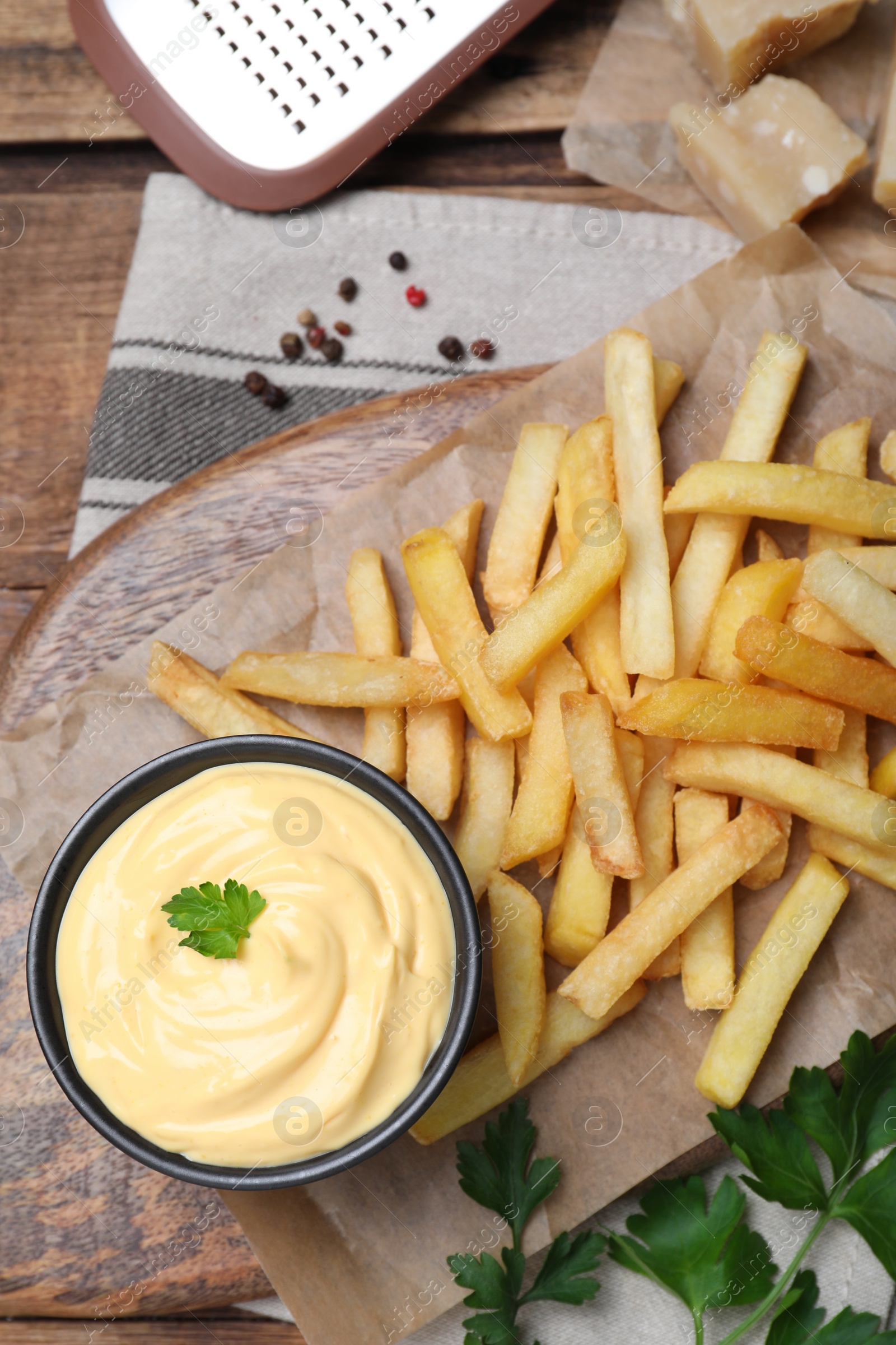 Photo of Delicious French fries and cheese sauce with parsley on wooden table, flat lay