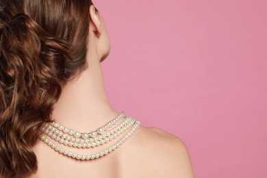 Photo of Young woman wearing elegant pearl necklace on pink background, back view. Space for text