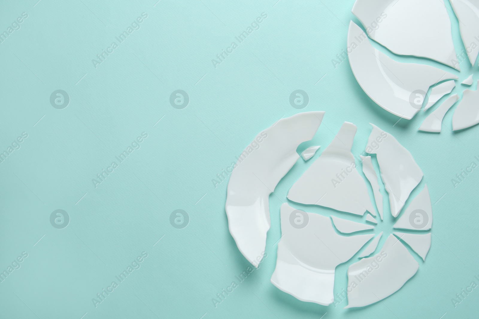 Photo of Two broken ceramic plates on light blue background, flat lay. Space for text