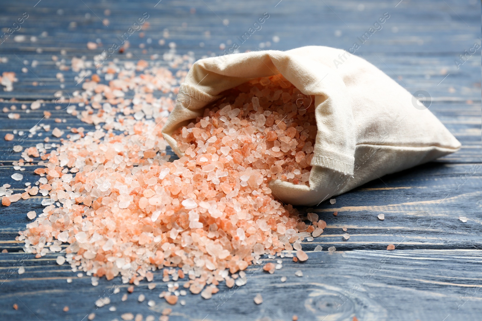 Photo of Overturned bag with pink himalayan salt on blue wooden table