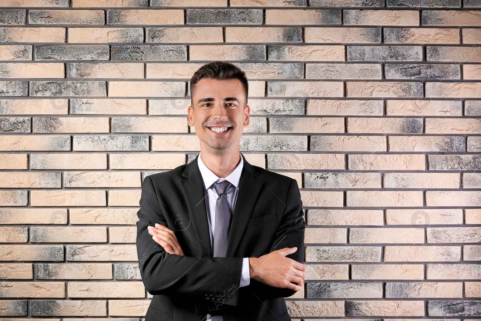 Photo of Handsome young man in suit near brick wall background