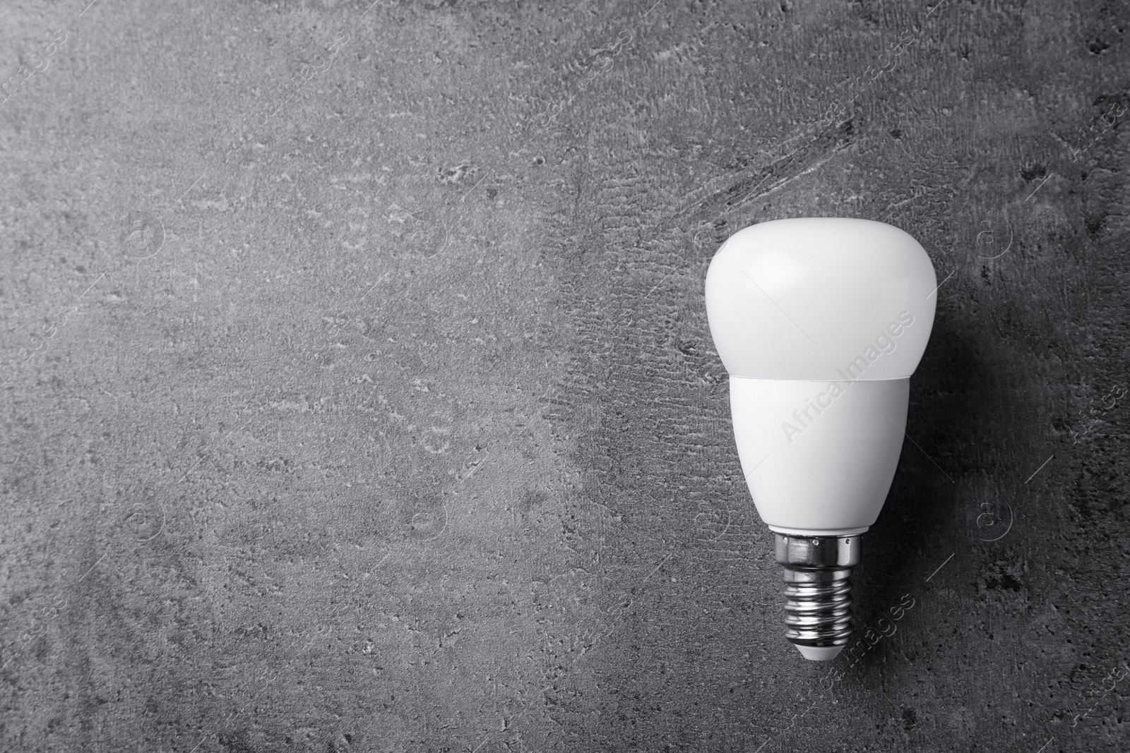 Photo of New modern lamp bulb on grey stone surface, top view. Space for text