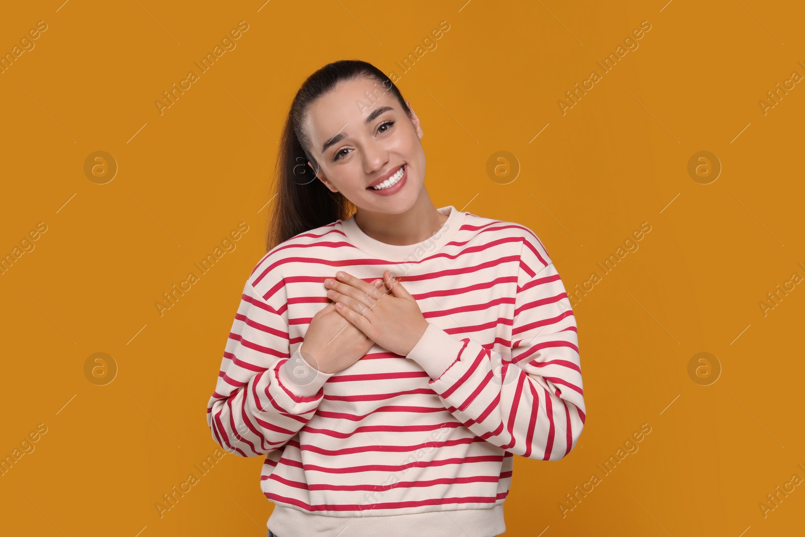 Photo of Thank you gesture. Beautiful grateful woman with hands on chest against orange background