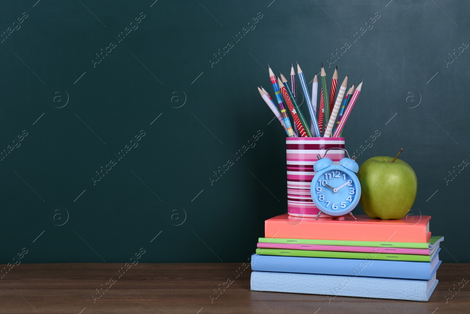 Photo of Composition with stationery, apple and alarm clock on table near chalkboard, space for text. Doing homework