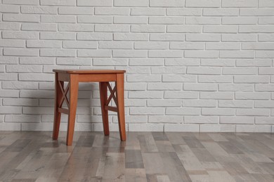 Stylish wooden stool near white brick wall indoors. Space for text