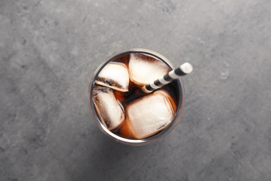 Glass of refreshing cola with ice on grey background, top view