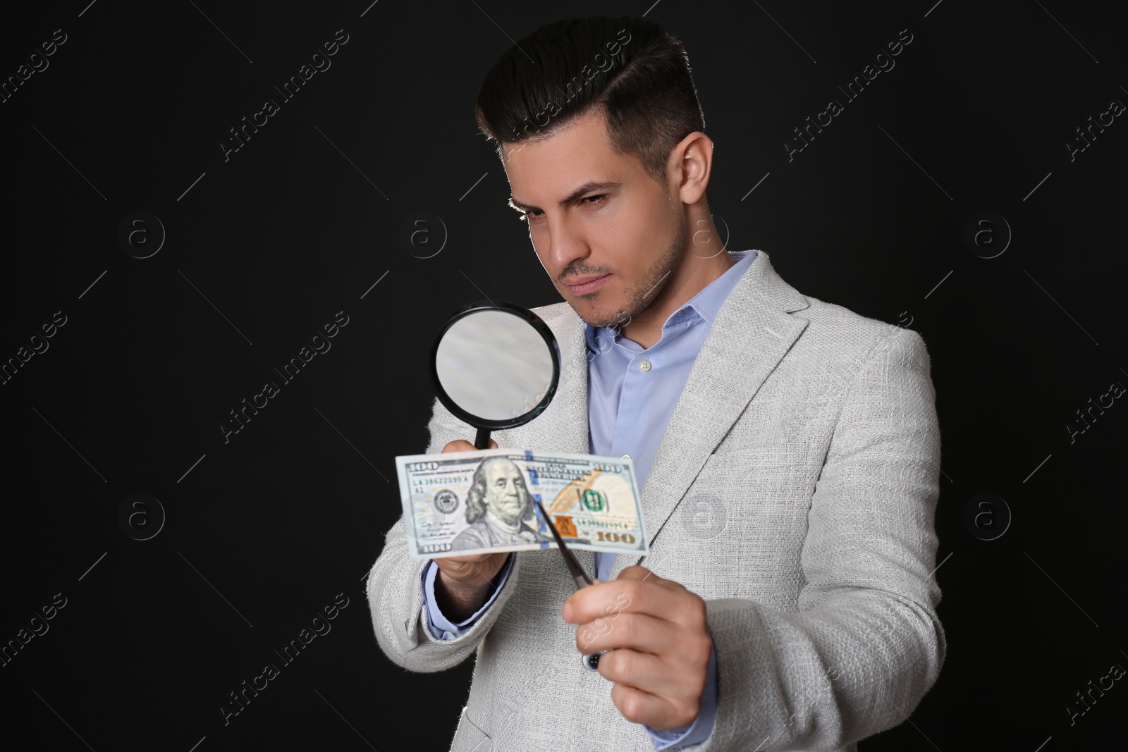Photo of Expert authenticating 100 dollar banknote with magnifying glass against black background. Fake money concept