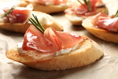 Photo of Tasty bruschettas with prosciutto and cream cheese on parchment, closeup