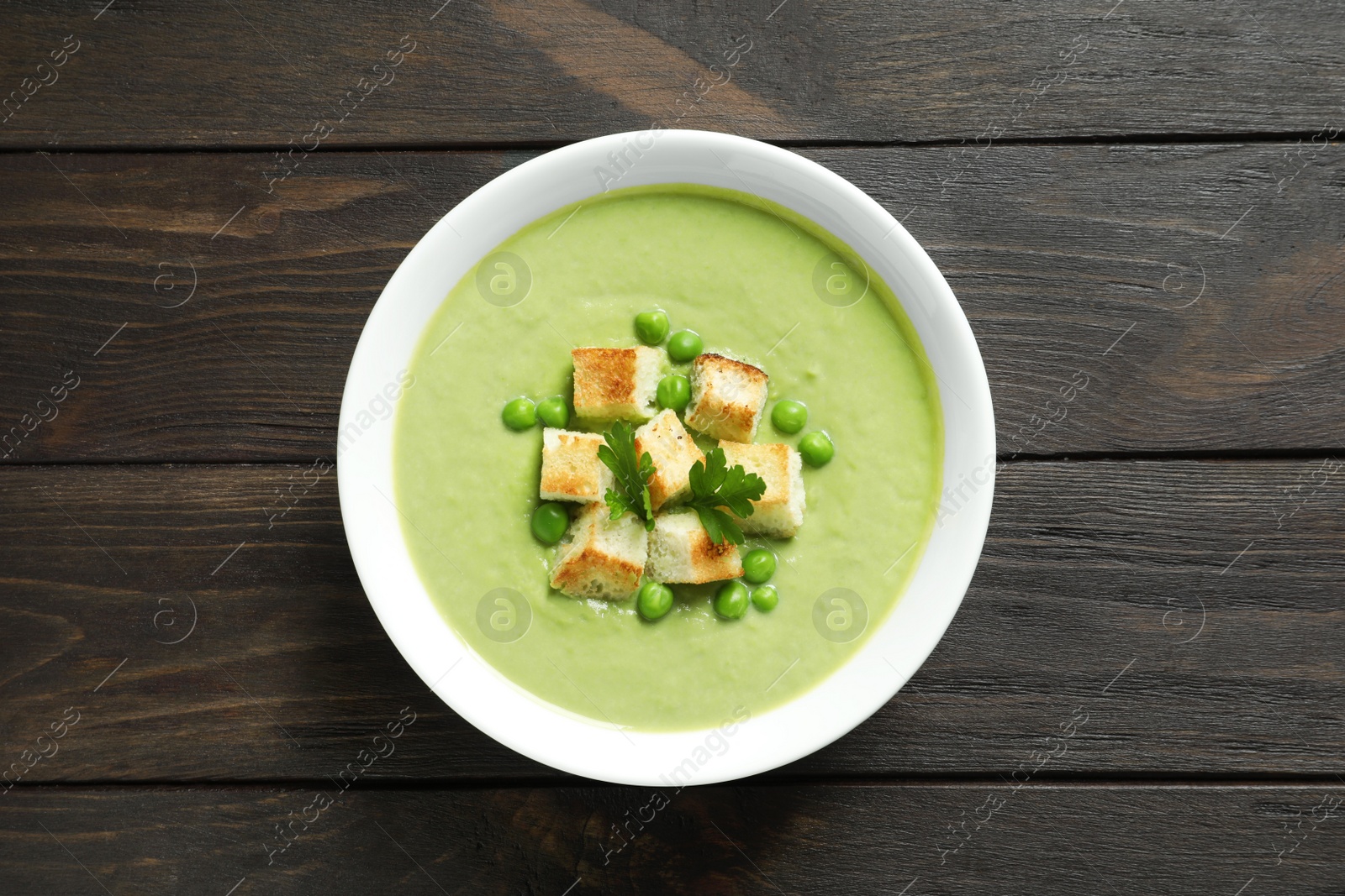 Photo of Fresh vegetable detox soup made of green peas with croutons in dish on wooden background, top view