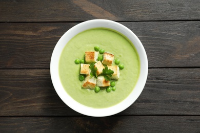 Fresh vegetable detox soup made of green peas with croutons in dish on wooden background, top view