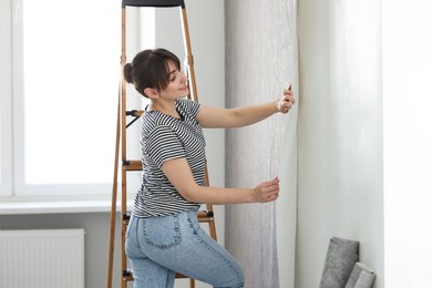 Photo of Woman hanging stylish gray wallpaper in room