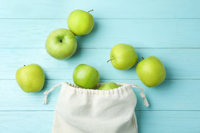 Photo of Cotton eco bag with apples on light blue wooden background, flat lay