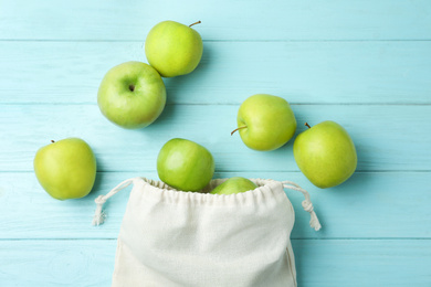 Cotton eco bag with apples on light blue wooden background, flat lay