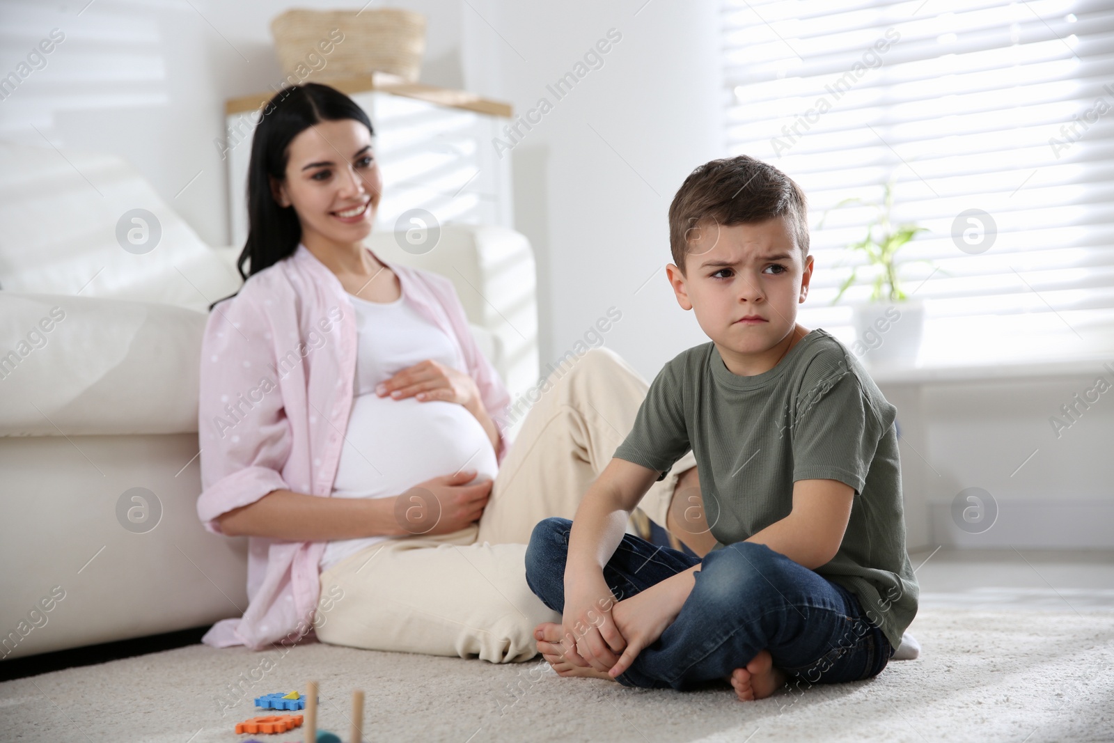 Photo of Unhappy little boy near pregnant mother at home. Feeling jealous towards unborn sibling