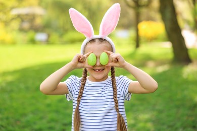 Photo of Easter celebration. Cute little girl in bunny ears covering eyes with painted eggs outdoors