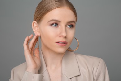 Beautiful young woman with elegant earrings on gray background