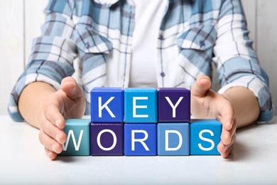 Photo of Woman demonstrating colorful cubes with word KEYWORDS at white table, closeup