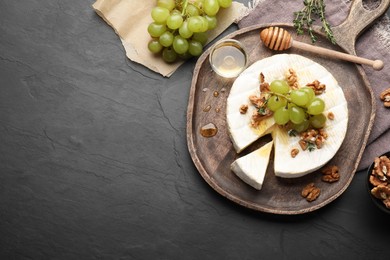 Photo of Brie cheese served with grapes, walnuts and honey on grey table, flat lay. Space for text
