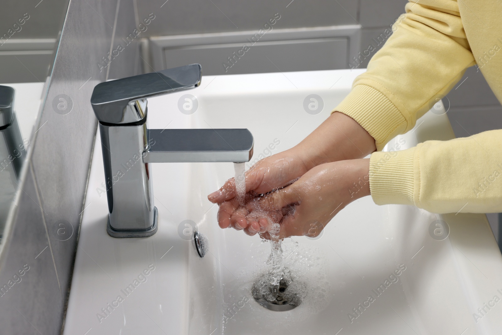 Photo of Woman washing hands with water from tap in bathroom, closeup