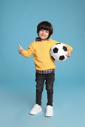 Photo of Cute little boy with soccer ball on light blue background