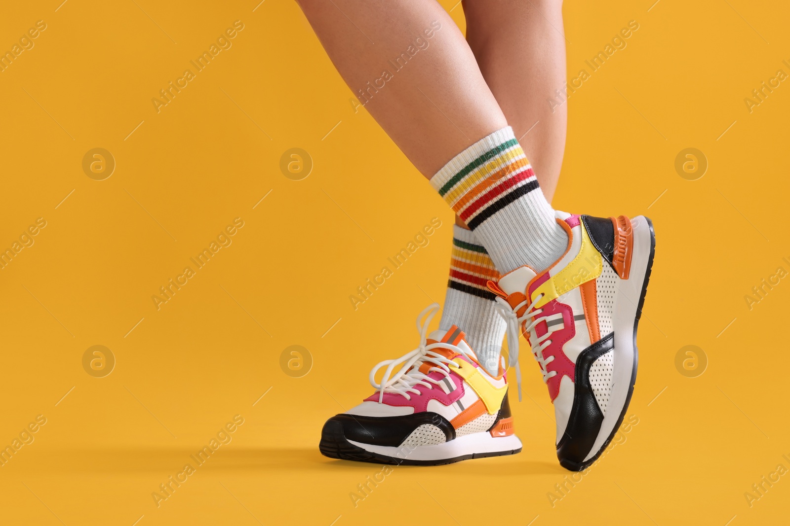 Photo of Woman wearing stylish sneakers on yellow background, closeup. Space for text