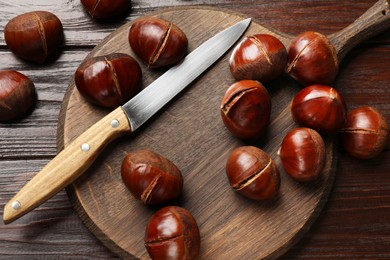 Photo of Roasted edible sweet chestnuts and knife on wooden table, flat lay