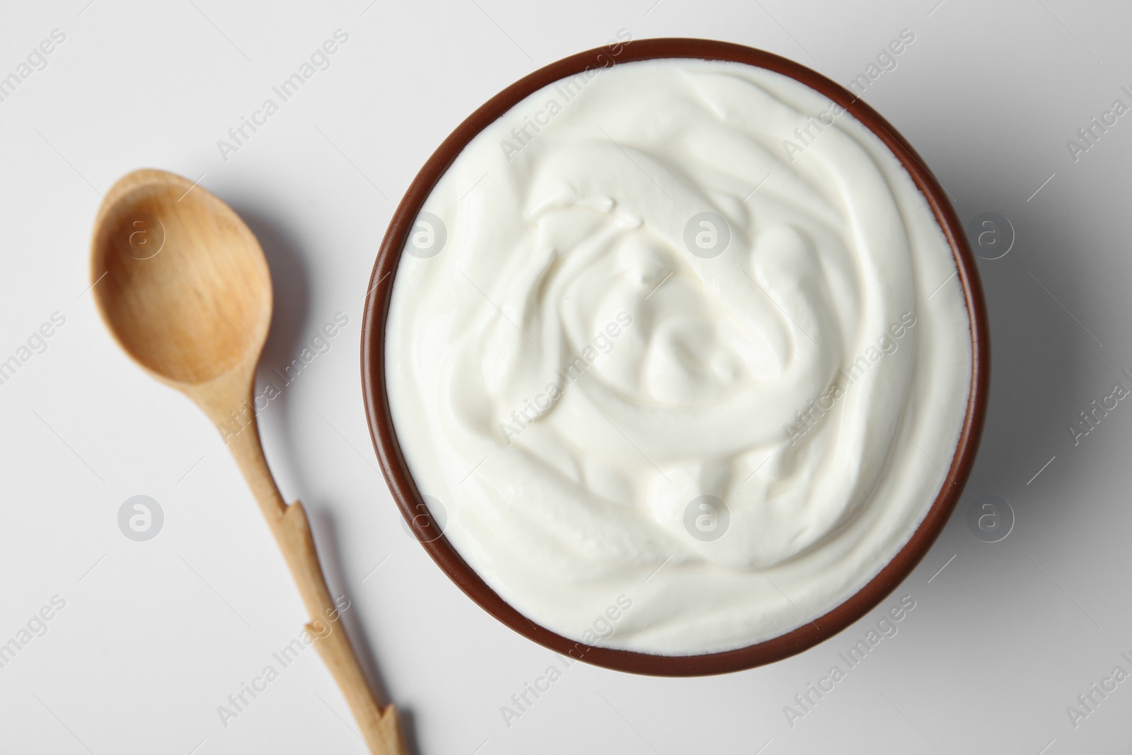 Photo of Bowl of sour cream and wooden spoon on white background, top view